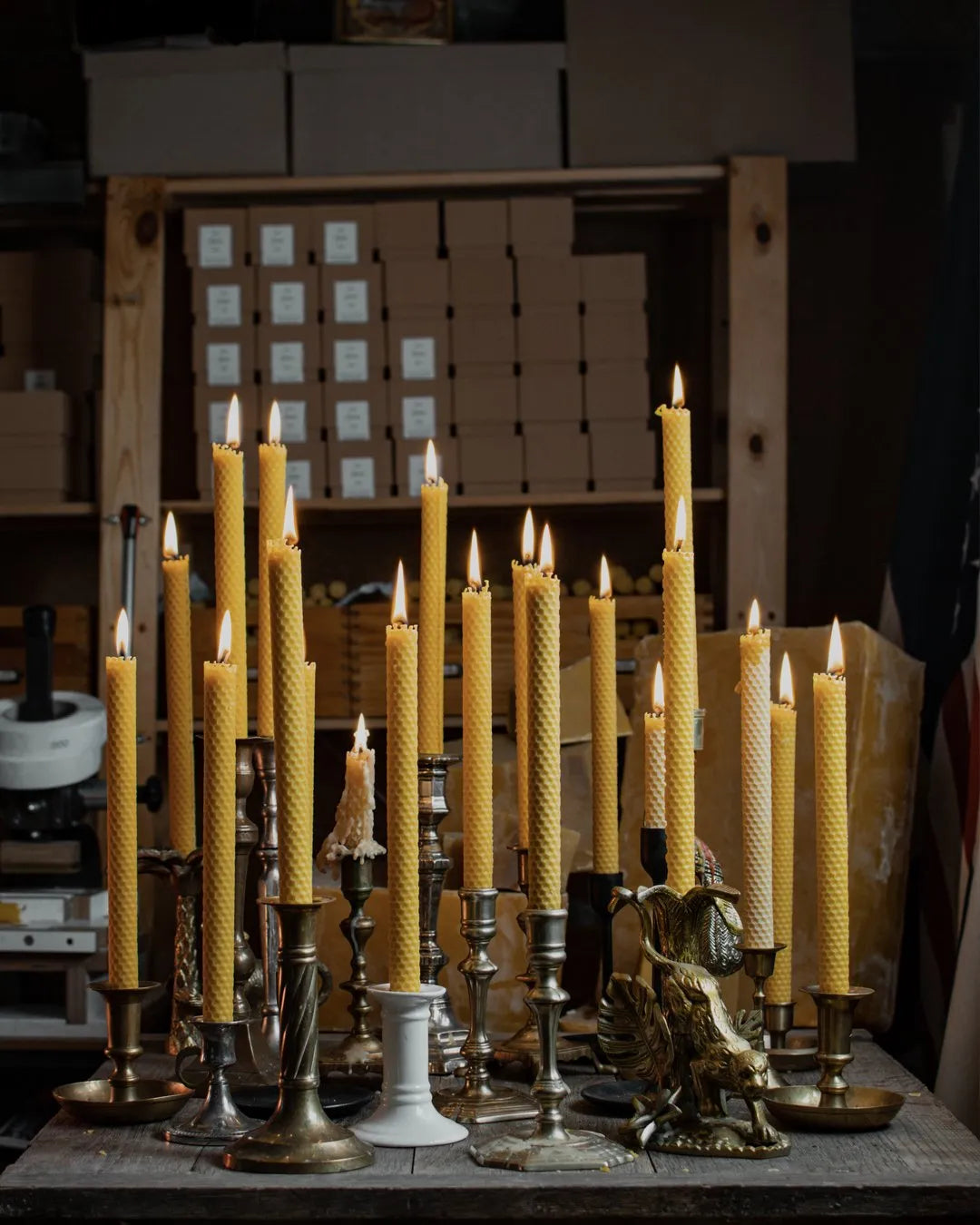 Plusieurs bougies Lucienne en cire d'abeille gaufrée allumées sur des bougeoirs anciens.