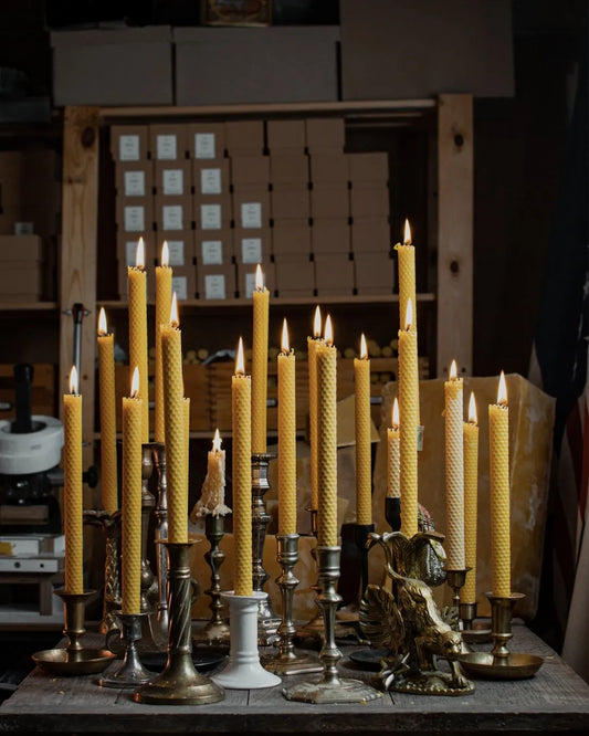 Plusieurs bougies Lucienne en cire d'abeille gaufrée allumées sur des bougeoirs anciens.